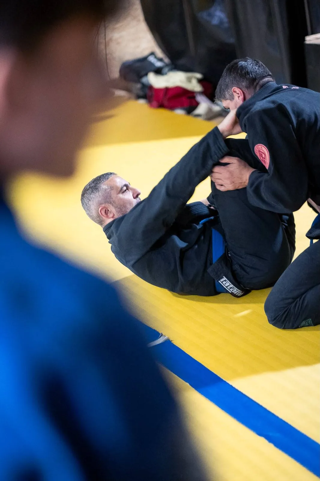 Entraînement de JJB chez Akela Jiu Jitsu à Rouen : deux pratiquants en kimono noir travaillent la garde sur les tatamis jaunes du club