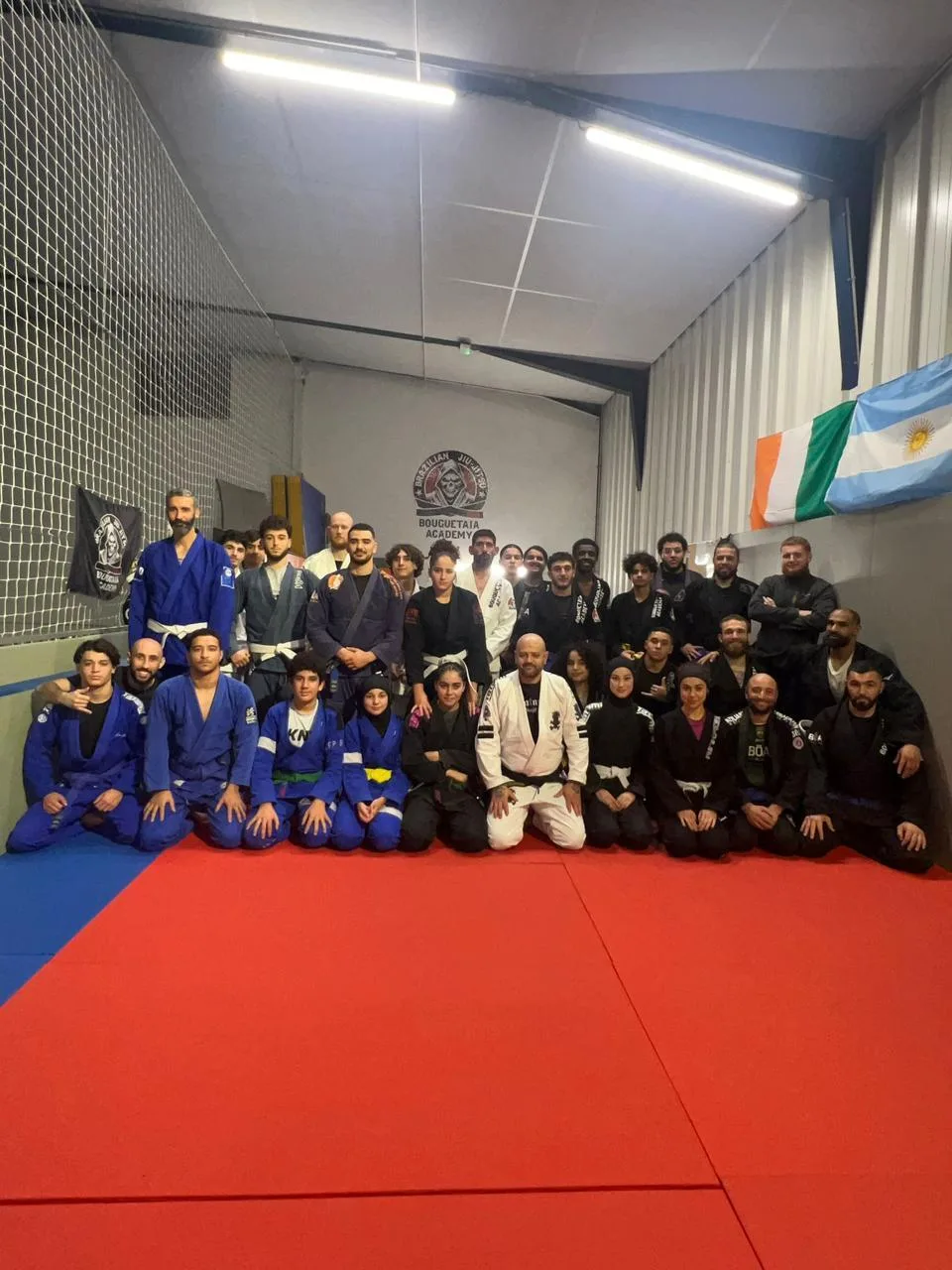 Le groupe d'élèves de la Bouguetaia Academy en kimono sur les tatamis du club à Nîmes, devant la bannière tête de mort du club