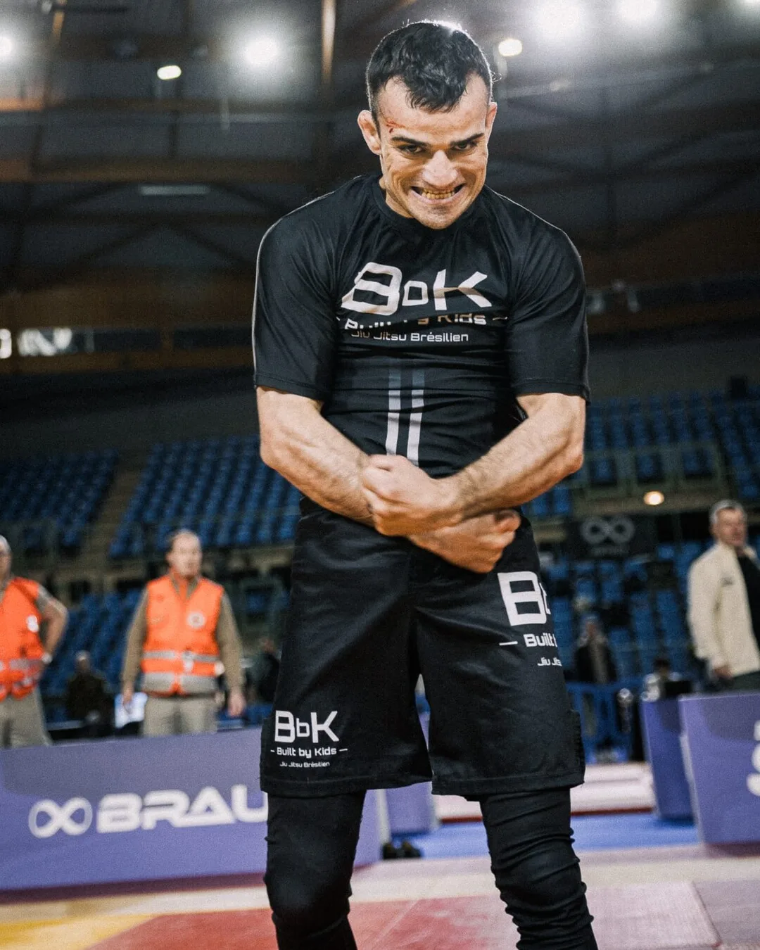 Compétiteur Built by Kids en rashguard BbK, poings serrés après un combat, dans la salle de compétition