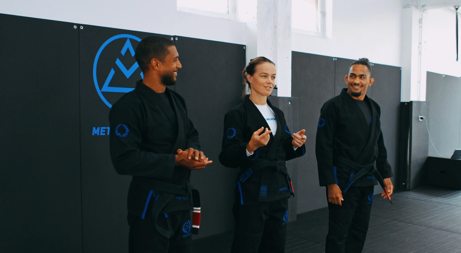 Nicolas Randriamihamina, Camilla Sæther et Alexandre Sidambarompoulle en kimono noir devant le mur au logo de Meta Jiu Jitsu, à Toulouse