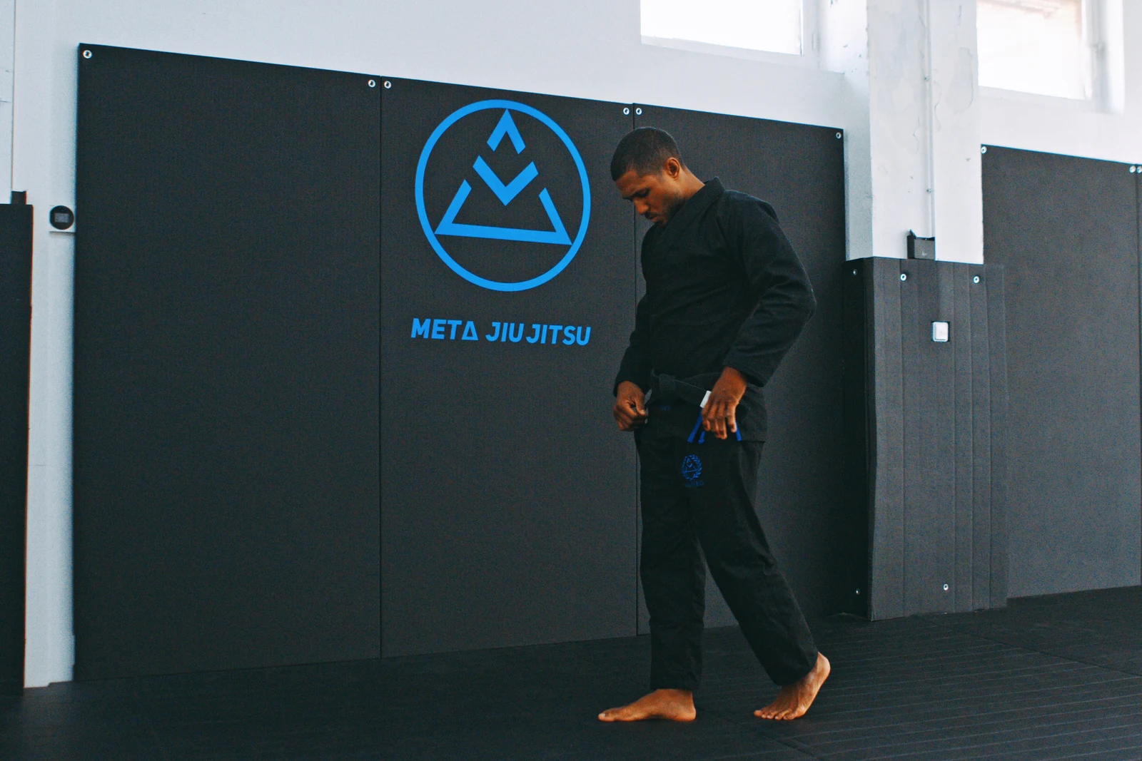 Un enseignant de Meta Jiu Jitsu ajuste sa ceinture devant le mur au logo du club