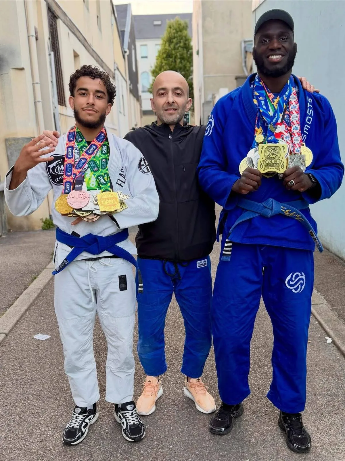 David Merkhi entouré de deux compétiteurs ceinture bleue de la MK Team Le Havre, les bras chargés de médailles de tournois de jiu-jitsu brésilien