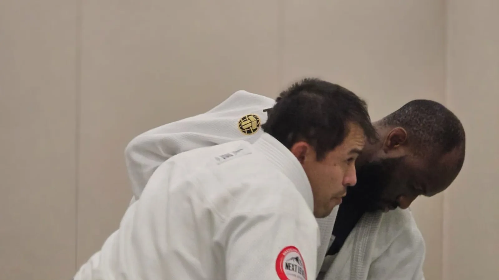 Deux pratiquants de Next Level Jiu Jitsu Besançon front contre front au sol en kimono, patch du club visible