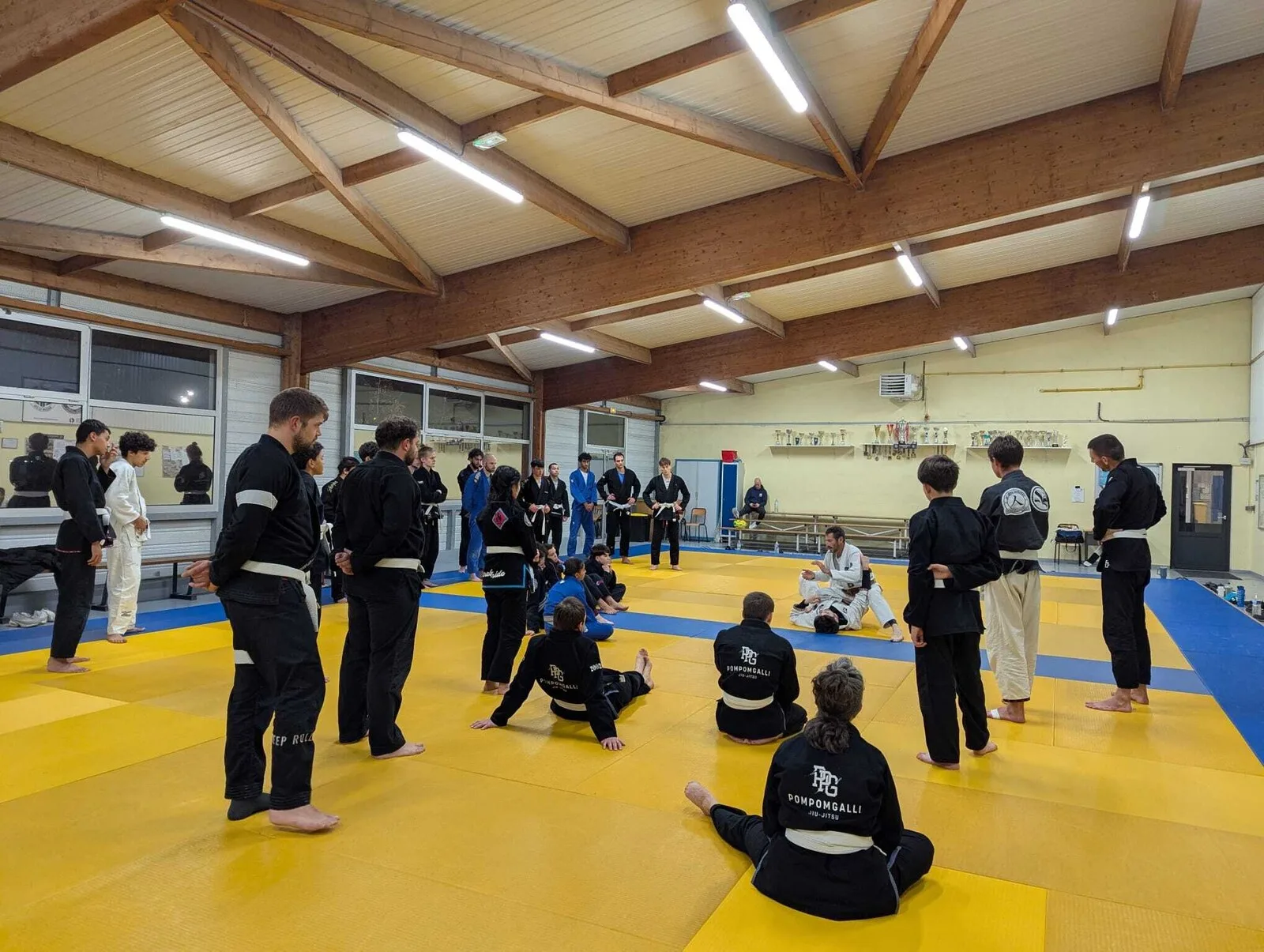 Cours de JJB à PomPomGalli Jiu-Jitsu : les élèves en kimono autour du coach qui démontre une technique au sol